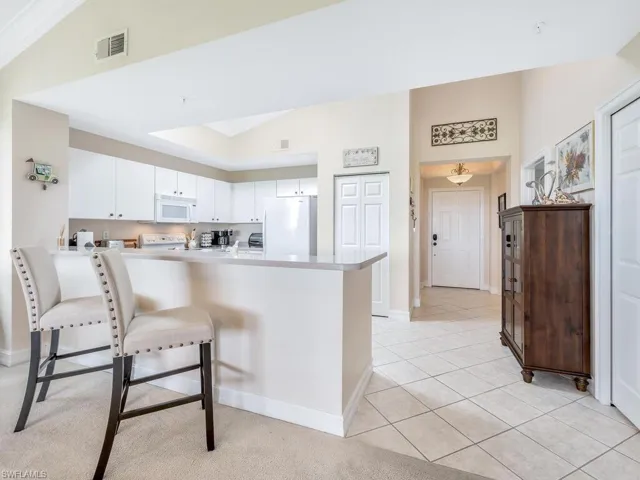 Kitchen with a breakfast bar area, white appliances, & white cabinets