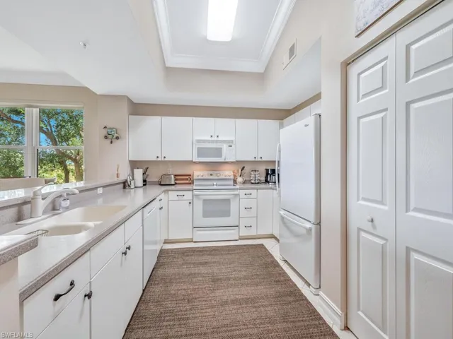 Kitchen featuring white cabinetry, a tray ceiling, white appliances, crown molding, and double sink