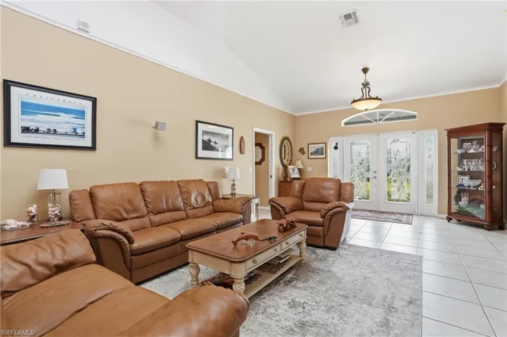 Living room featuring vaulted ceiling, french doors, light tile patterned flooring, and crown molding