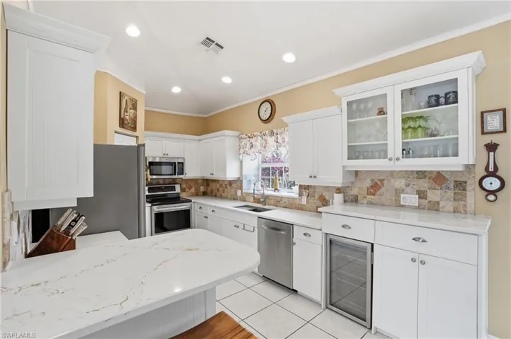 Kitchen featuring white cabinetry, glass fronted cabinets, beverage cooler, stainless steel appliances, and light tile patterned floors