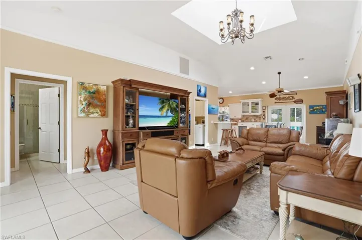 Living area featuring light tile patterned floors, hanging lights, ceiling fan, and vaulted ceiling
