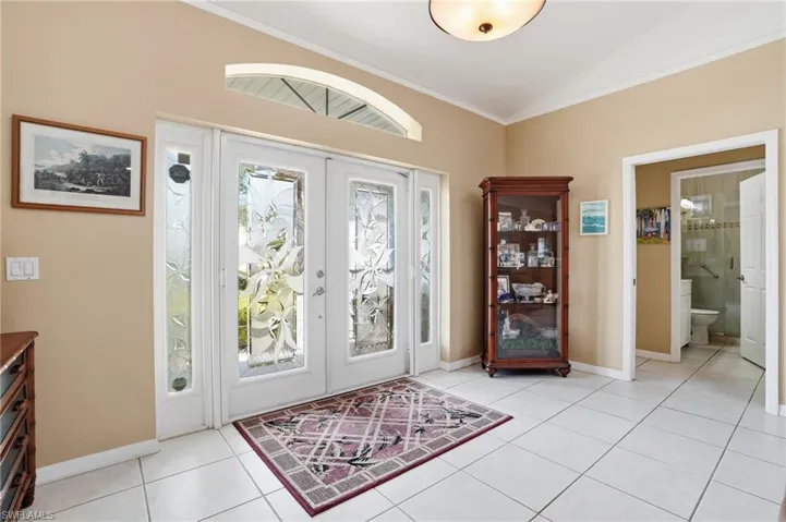 Entryway with french doors, crown molding, lofted ceiling, and light tile patterned floors