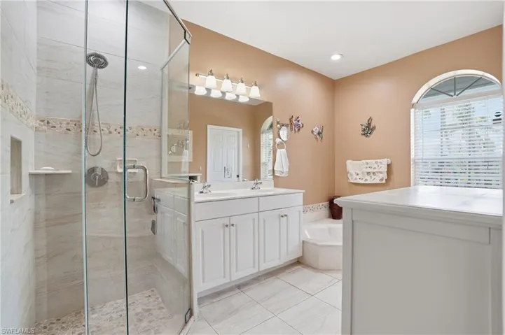 Bathroom featuring a stall shower, double vanity, light tile patterned flooring, and a bath