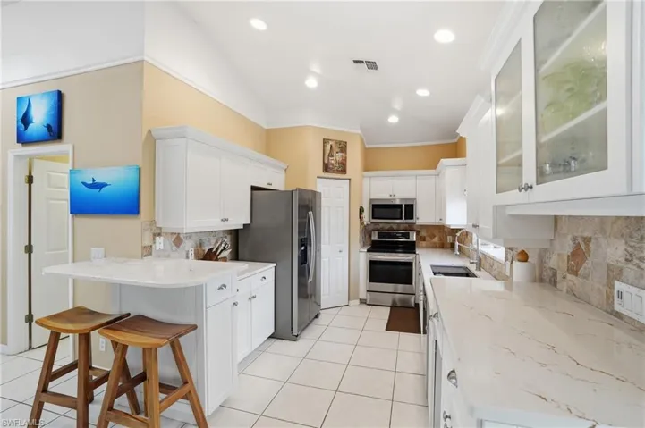 Kitchen with white cabinets, tasteful backsplash, glass insert cabinets, stainless steel appliances, and vaulted ceiling