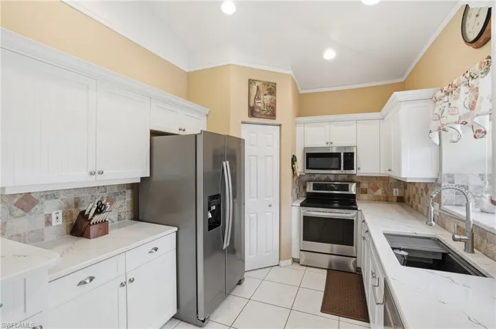 Kitchen with decorative backsplash, stainless steel appliances, light stone counters, ornamental molding, and lofted ceiling