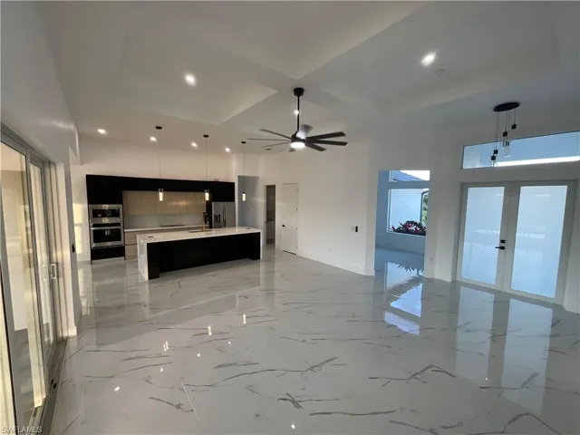 Kitchen featuring a center island with sink, pendant lighting, stainless steel refrigerator with ice dispenser, and coffered ceiling