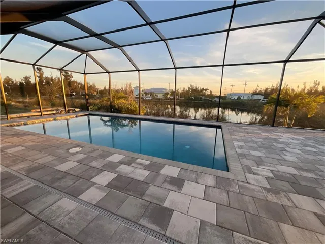 Pool at dusk with a patio area, a lanai, and a water view