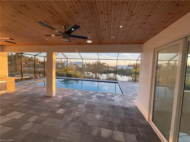 Pool at dusk with a patio, a water view, glass enclosure, and ceiling fan