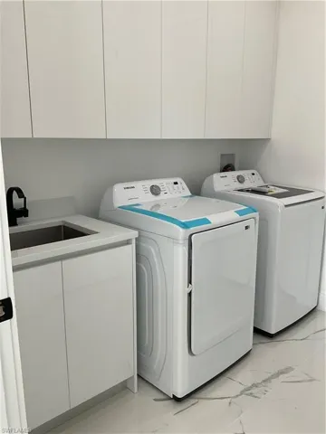 Clothes washing area featuring cabinets, washing machine and dryer, and sink