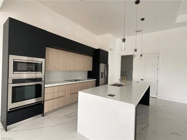Kitchen with appliances with stainless steel finishes, sink, light brown cabinets, decorative light fixtures, and an island with sink