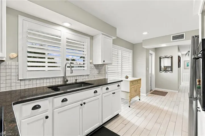 White cabinetry with black hardware, dark countertops, a tiled backsplash, plantation shutters, and light wood-finish flooring