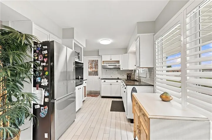 White cabinetry with dark countertops, white wood-finish flooring, plantation shutters, and a mosaic tile backsplash