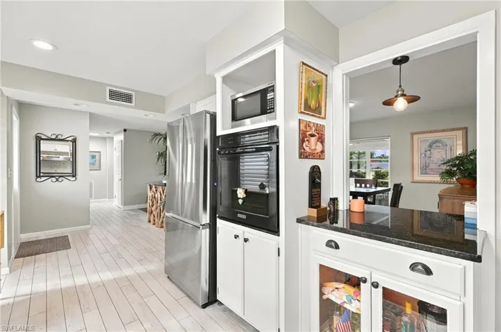 Kitchen featuring a stainless steel refrigerator, built-in wall oven and microwave, white cabinetry with dark hardware, and dark countertop