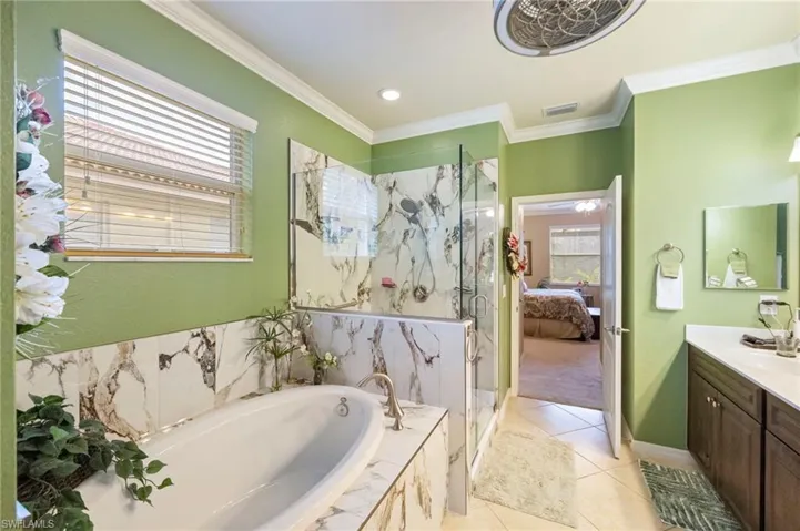 Full bath with a garden tub, vanity, a marble finish shower, ensuite bath, and ornamental molding