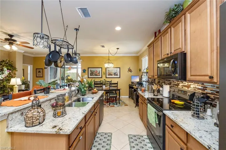 Kitchen with black appliances, light stone counters, decorative light fixtures, wood finish cabinetry, and light tile patterned flooring