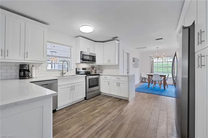 Kitchen featuring light stone counters, stainless steel appliances, white cabinetry, and wood tiled floors