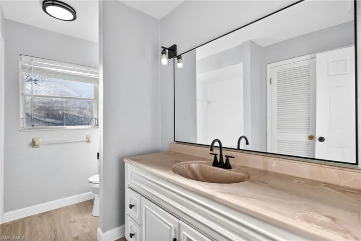 Bathroom featuring a spacious vanity with integrated sink, a large mirror, and wood-finish flooring