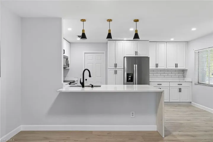 Modern kitchen featuring white shaker cabinetry, stainless steel appliances, a white subway tile backsplash, and a large central island with a matte black faucet
