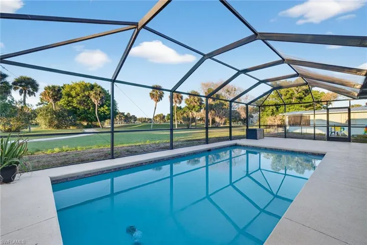 Screened-in pool deck featuring a geometric-shaped swimming pool with a tiled edge, concrete pool deck, and a transparent screen enclosure
