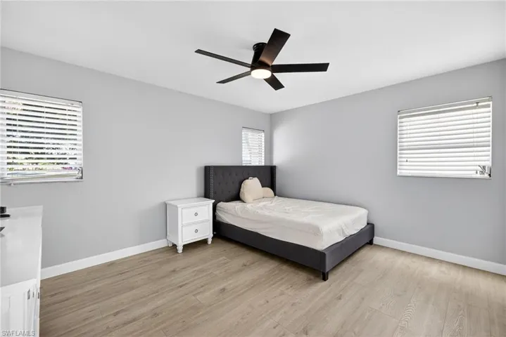 Spacious room featuring wood-finish flooring, light gray walls, a modern ceiling fan with integrated lighting, and two windows with horizontal blinds