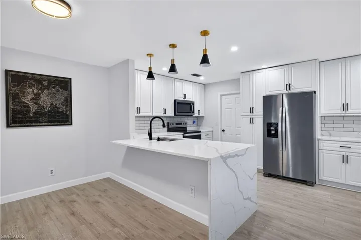 Kitchen featuring a waterfall-edge island with seating, white shaker cabinetry, stainless steel appliances, and a subway tile backsplash
