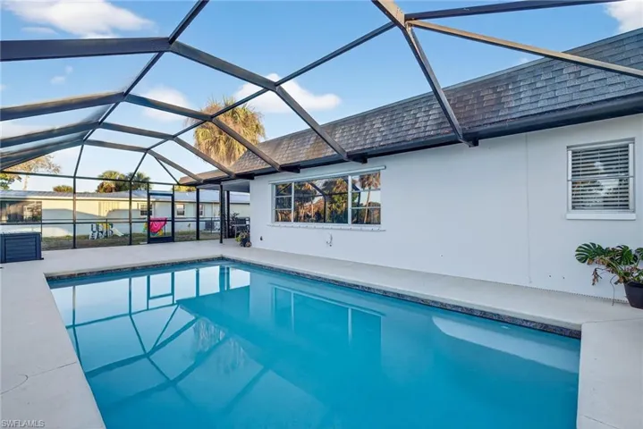 Screened outdoor pool with a dark blue tile border, light-colored pool deck, and white stucco exterior wall