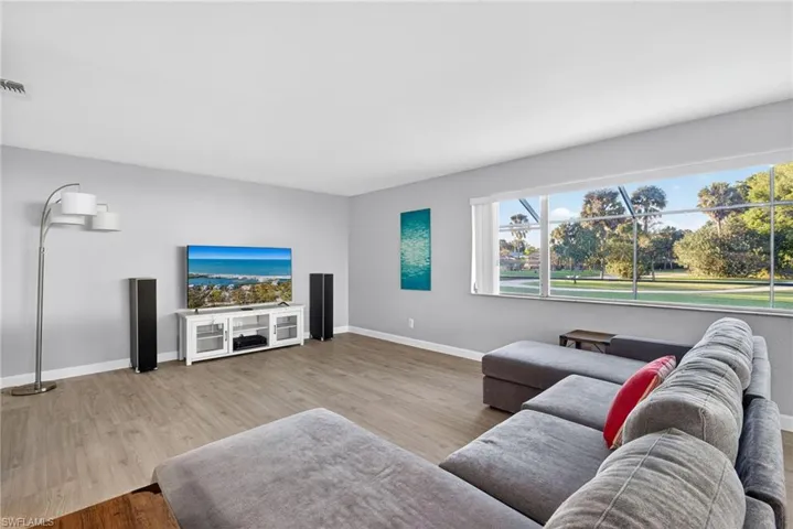 Spacious interior room featuring expansive window, wood-finish flooring, light gray walls, and white baseboards