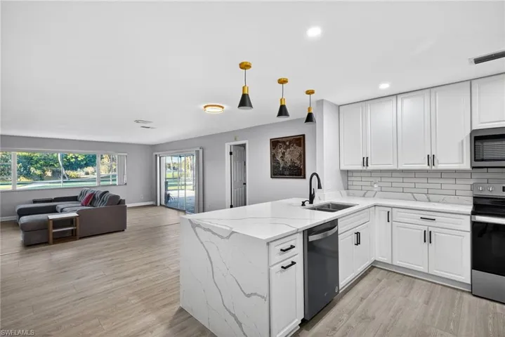 Modern kitchen featuring a waterfall island with a quartz countertop, white cabinetry with matte black hardware, and a subway tile backsplash