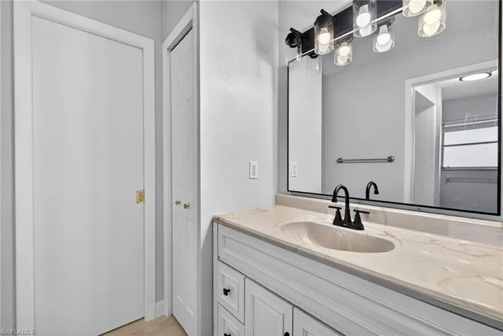 White vanity with an integrated sink and light-toned countertop, complemented by a black frame mirror and a multi-bulb vanity light fixture