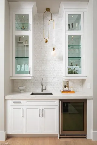 Bar featuring wine cooler, sink, tasteful backsplash, and light hardwood / wood-style flooring