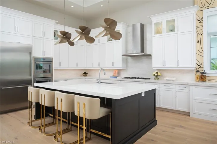 Kitchen with light hardwood / wood-style floors, stainless steel appliances, wall chimney exhaust hood, decorative light fixtures, and ceiling fan