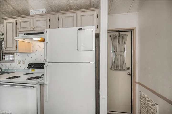 Kitchen featuring white appliances, light wood finish cabinetry, light countertops, and a textured ceiling