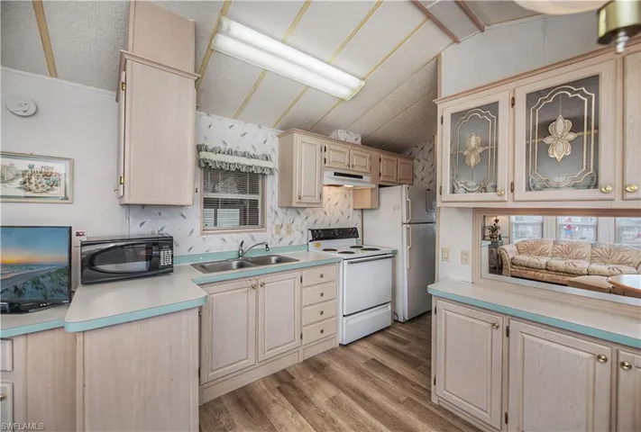 Kitchen featuring light countertops, white appliances, glass insert cabinets, light wood finish cabinets, and vaulted ceiling