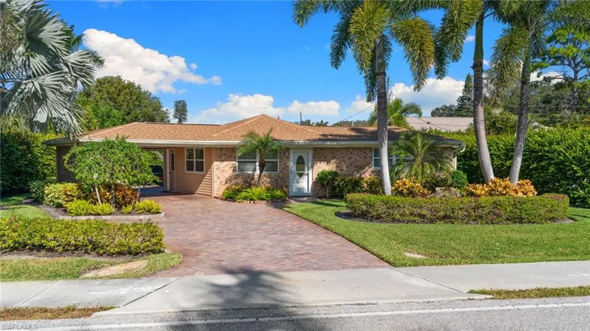 Single story, ranch-style home featuring a front yard, brick siding, decorative driveway, a carport, and roof with shingles