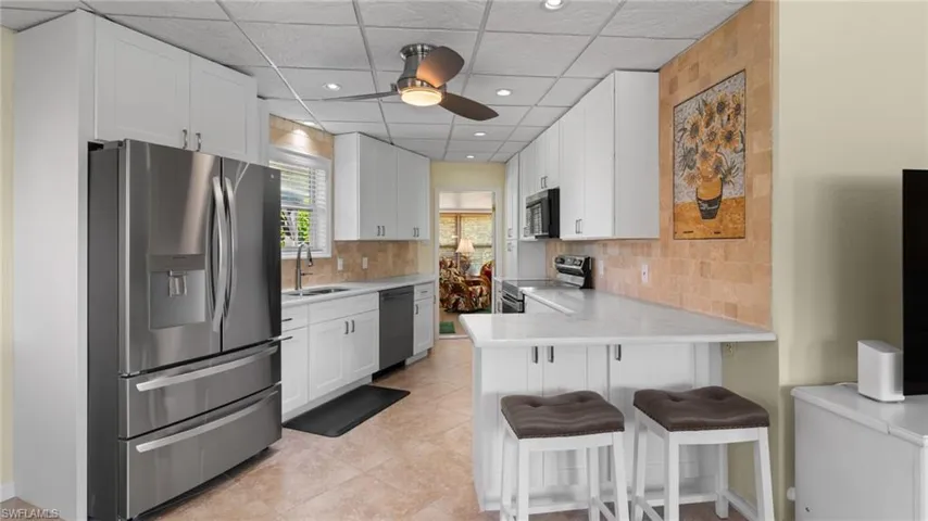 Kitchen featuring appliances with stainless steel finishes, a paneled ceiling, a breakfast bar, a peninsula, and light tile patterned floors