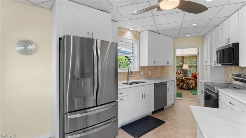 Kitchen featuring stainless steel appliances, a drop ceiling, light stone countertops, white cabinets, and light tile patterned flooring