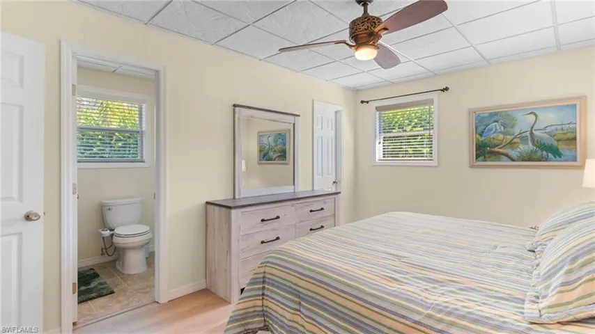 Bedroom featuring multiple windows, ceiling fan, ensuite bath, a paneled ceiling, and light wood finished floors
