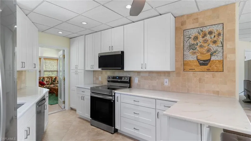 Kitchen with appliances with stainless steel finishes, white cabinets, decorative backsplash, light tile patterned flooring, and a drop ceiling