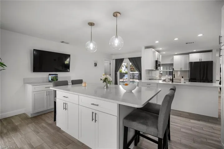 Kitchen featuring black fridge, white cabinets, light hardwood / wood-style flooring, pendant lighting, and a large island with sink