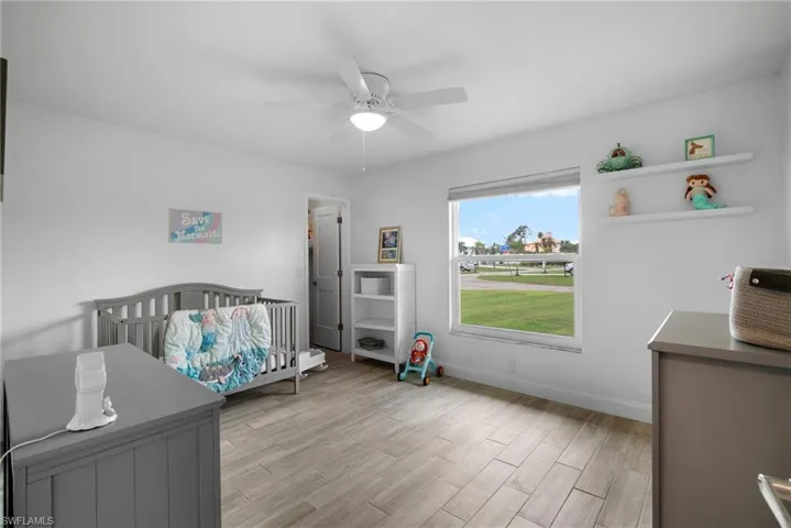 Bedroom featuring light hardwood / wood-style floors, ceiling fan, and a crib