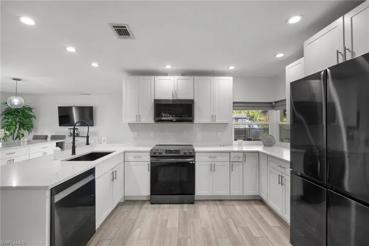 Kitchen featuring black appliances, white cabinetry, light wood-type flooring, sink, and kitchen peninsula