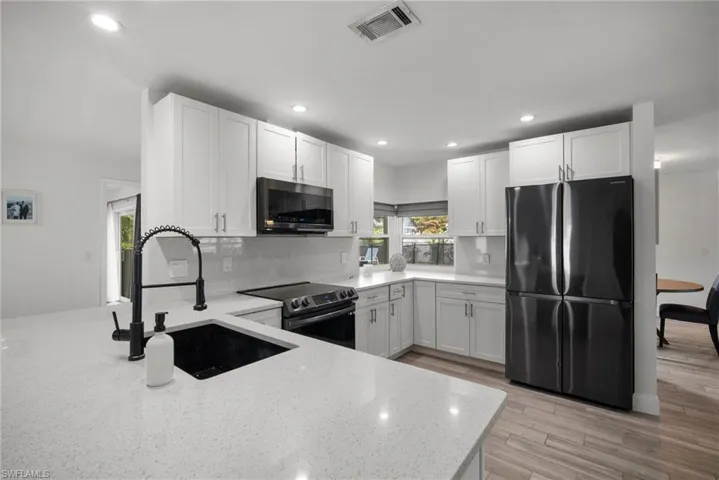 Kitchen featuring stainless steel appliances, light stone counters, white cabinets, sink, and light wood-type flooring