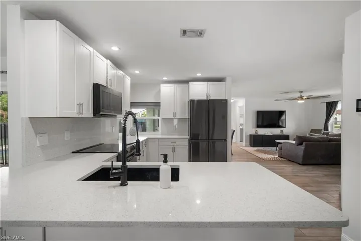 Kitchen featuring white cabinetry, light stone counters, appliances with stainless steel finishes, ceiling fan, and light hardwood / wood-style flooring