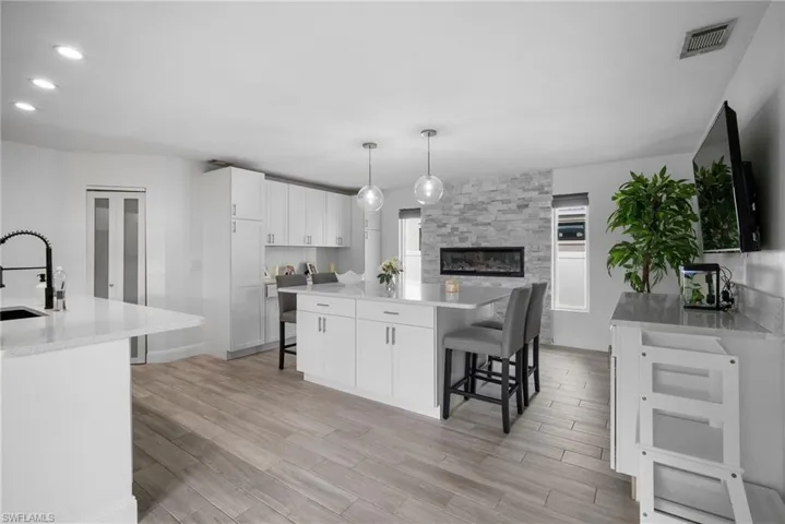 Kitchen with a stone fireplace, a kitchen island, pendant lighting, light hardwood / wood-style floors, and white cabinets