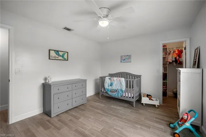 Bedroom featuring a closet, a nursery area, a spacious closet, light wood-type flooring, and ceiling fan