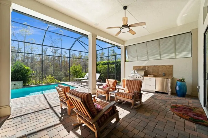 Covered patio with an outdoor kitchen setup and seating, which opens to the pool deck through large sliding glass doors.