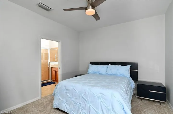 Bedroom with light colored carpet, connected bathroom, and ceiling fan