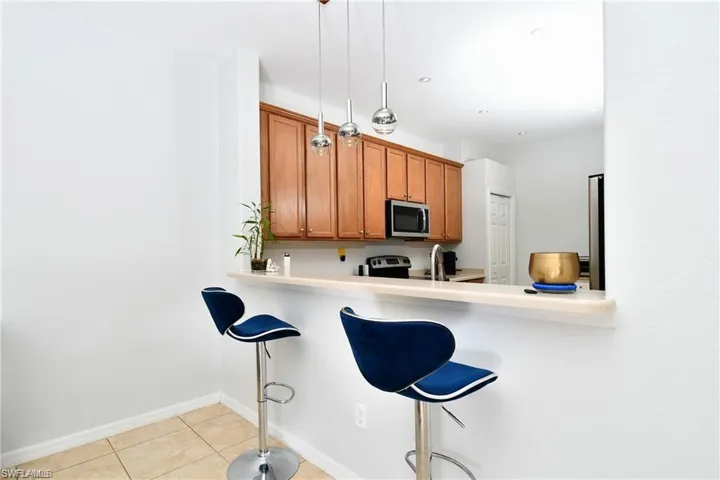 Kitchen with light tile patterned floors, sink, kitchen peninsula, pendant lighting, and a breakfast bar