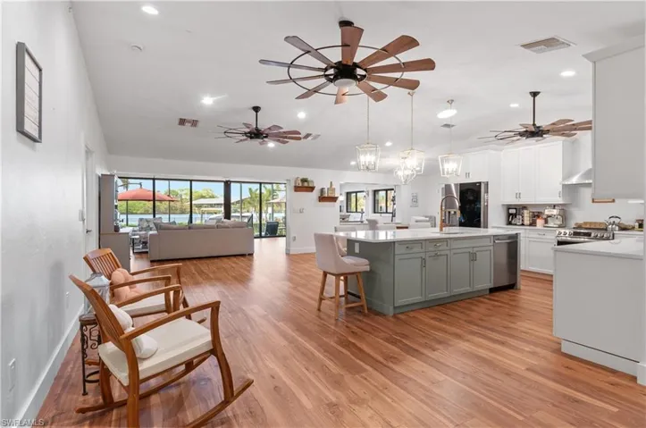 Kitchen featuring a breakfast bar, a center island with sink, a ceiling fan, decorative light fixtures, and high vaulted ceiling