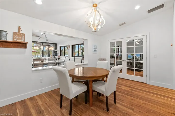 Dining area with a chandelier, vaulted ceiling, french doors, wood finished floors, and recessed lighting